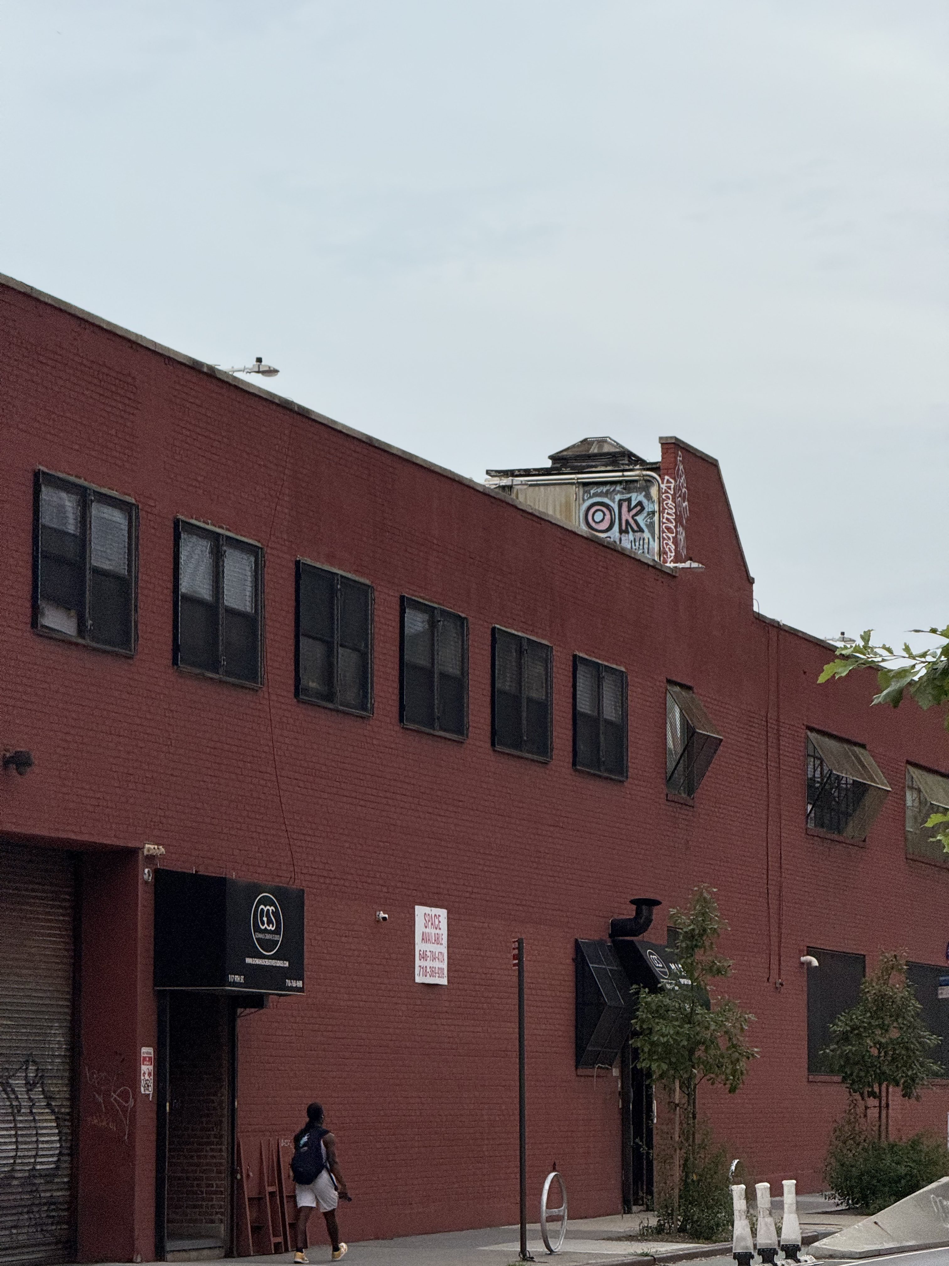 person walking outside a red brick building whose small chimney has been graffitied to say "ok"
