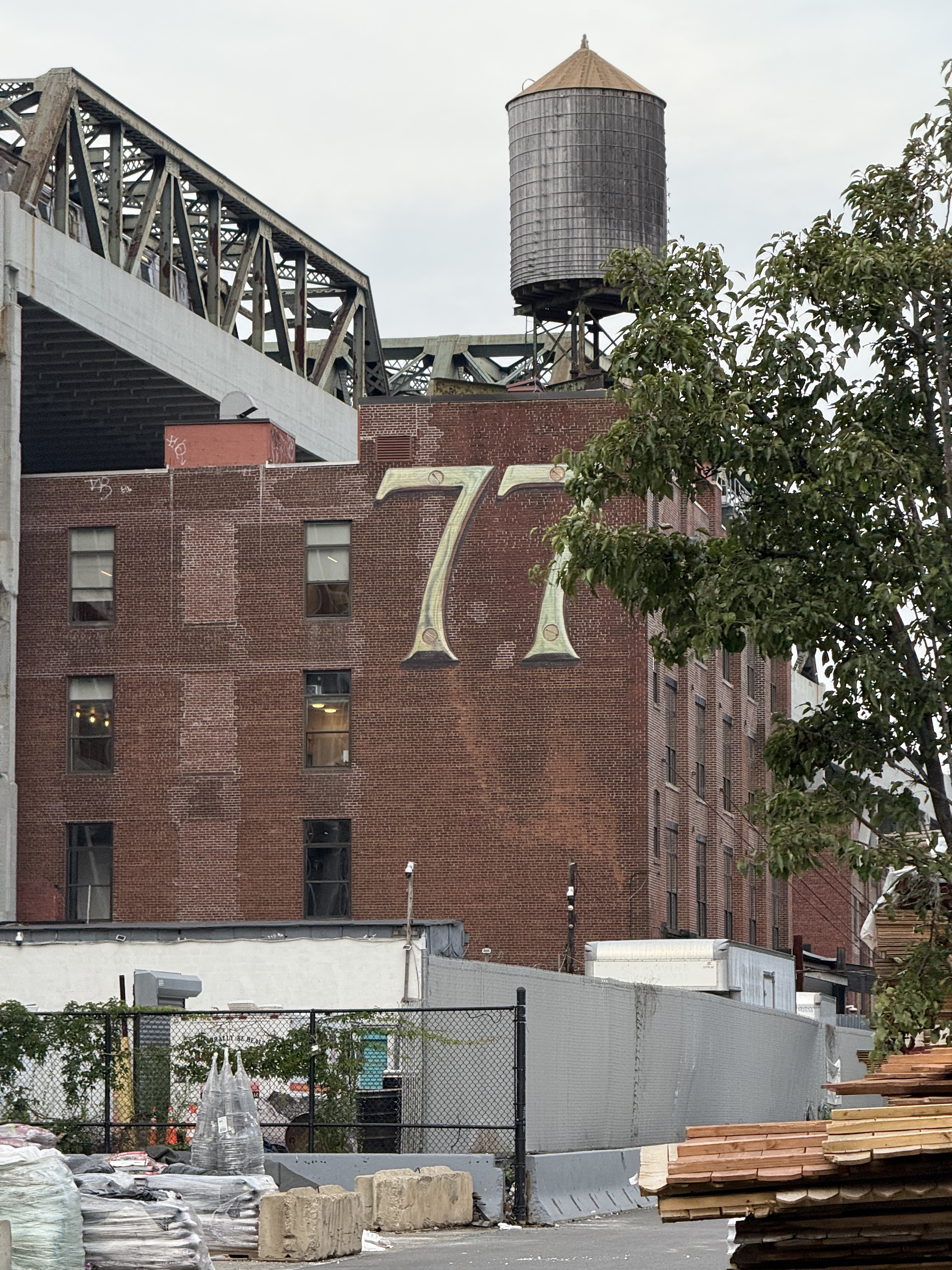 slightly dilapidated red brick building with faux industrial metal 77 painted on it nevertheless has real industry going on around with, with piles of various construction materials at its base and a train running overhead