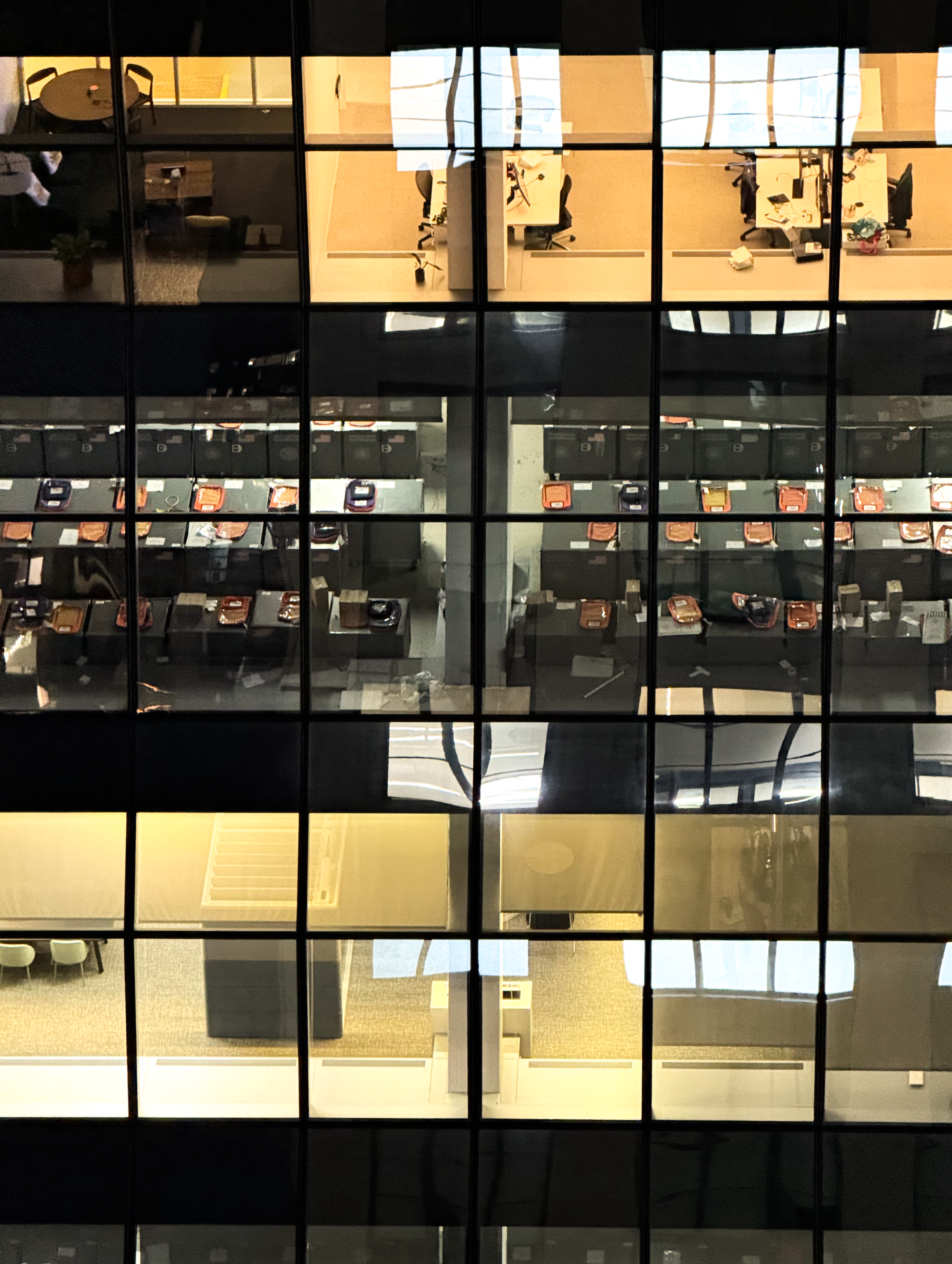 various office building cubicles, as viewed from above & outside the building. slight imperfections in the glass make each yellow-LED-lit office seem warped, despite the perfectly straight grid of window borders.