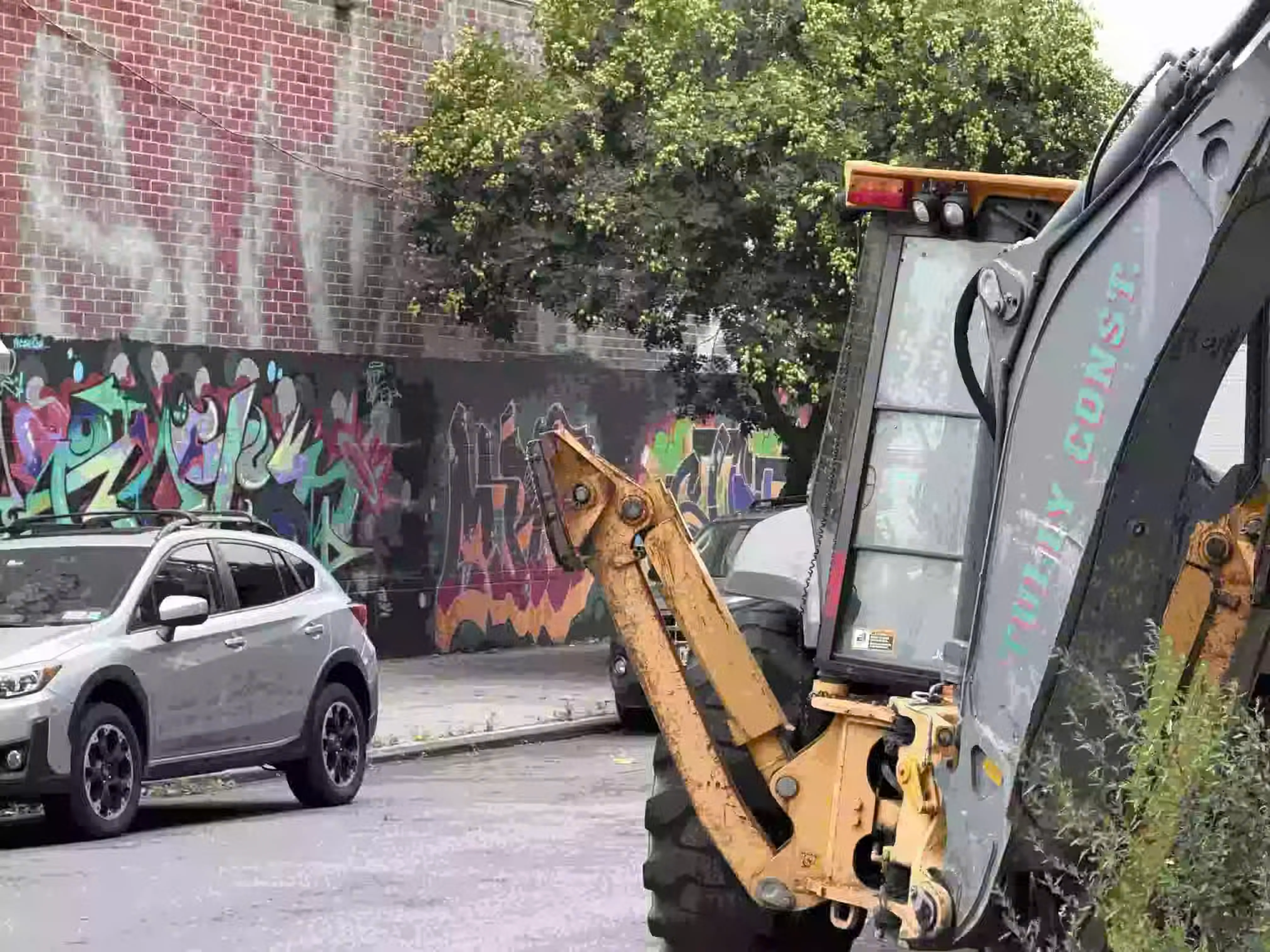 An excavator, light SUV, and graffiti are all lightly touched by compression artifacts, the colors unnaturally saturated