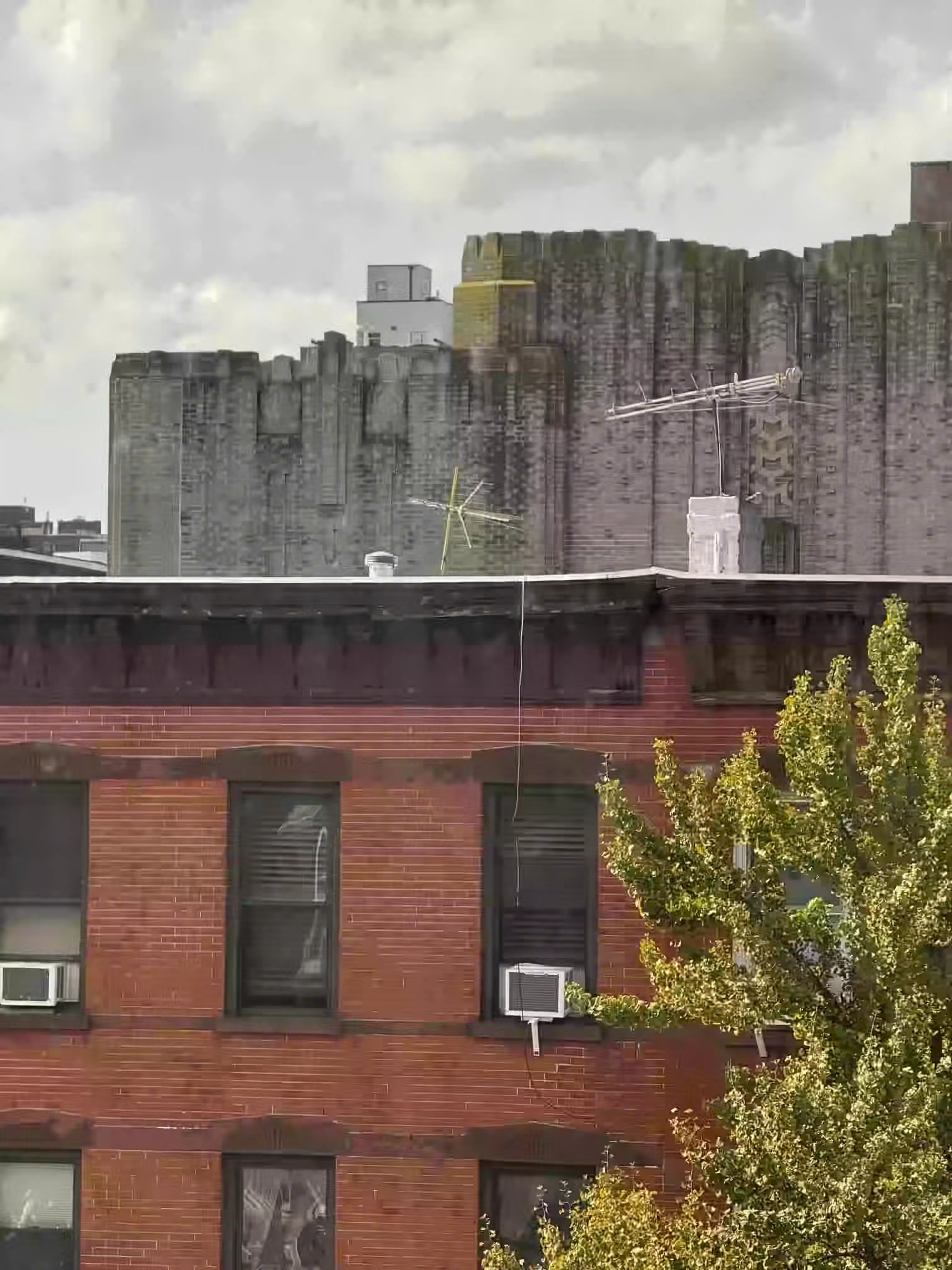 Straight-on view of a brownstone rooftop against a slightly taller gray brick building and a blocky sky