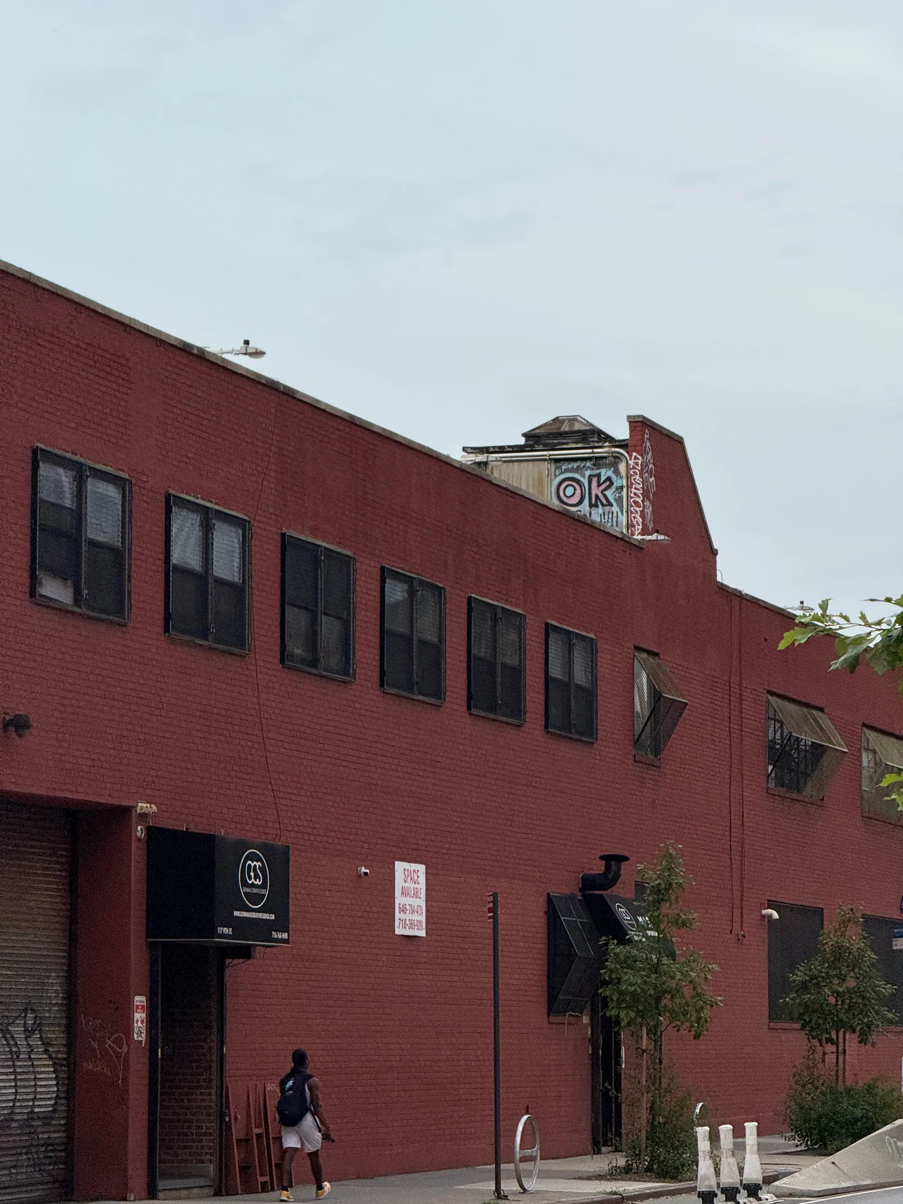 person walking outside a red brick building whose small chimney has been graffitied to say "ok"