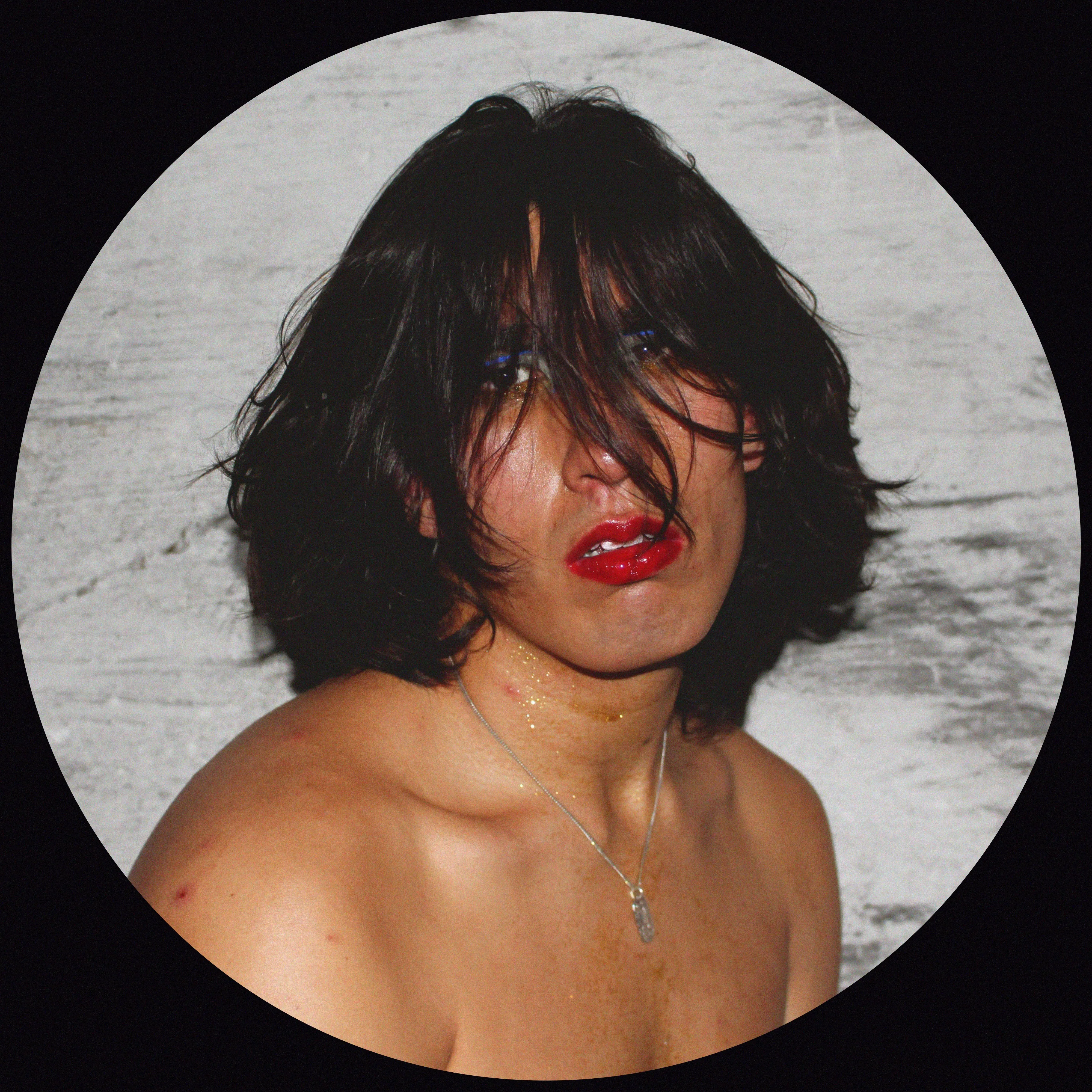 A clocky Trans woman with slightly disheveled hair & makeup gazes shirtlessly at the camera